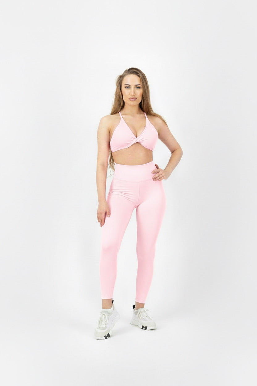 Woman wearing a pink sports bra and leggings on a white background